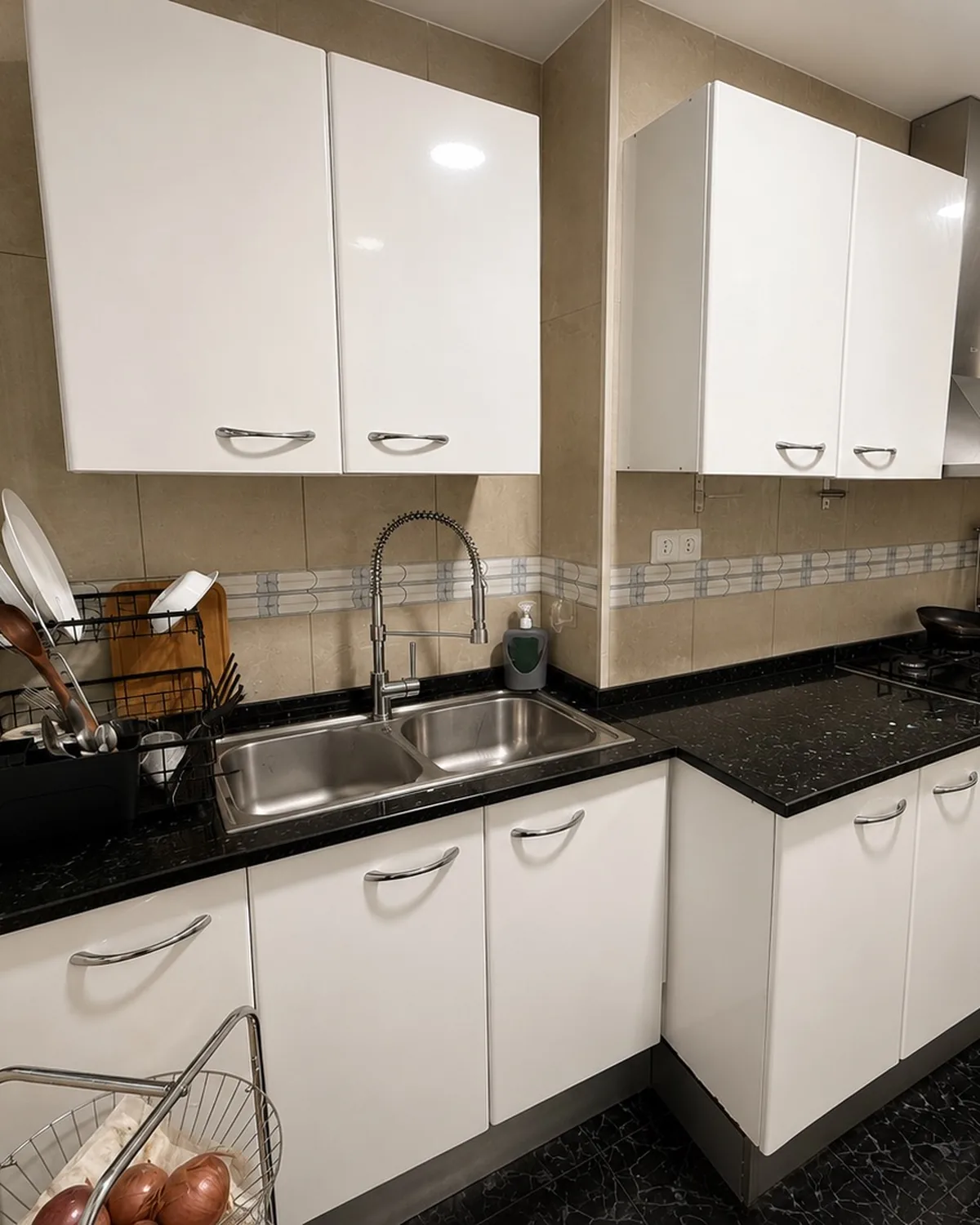 Cocina antes de la reforma, con muebles blancos de tiradores cromados, encimera negra y fregadero de dos senos