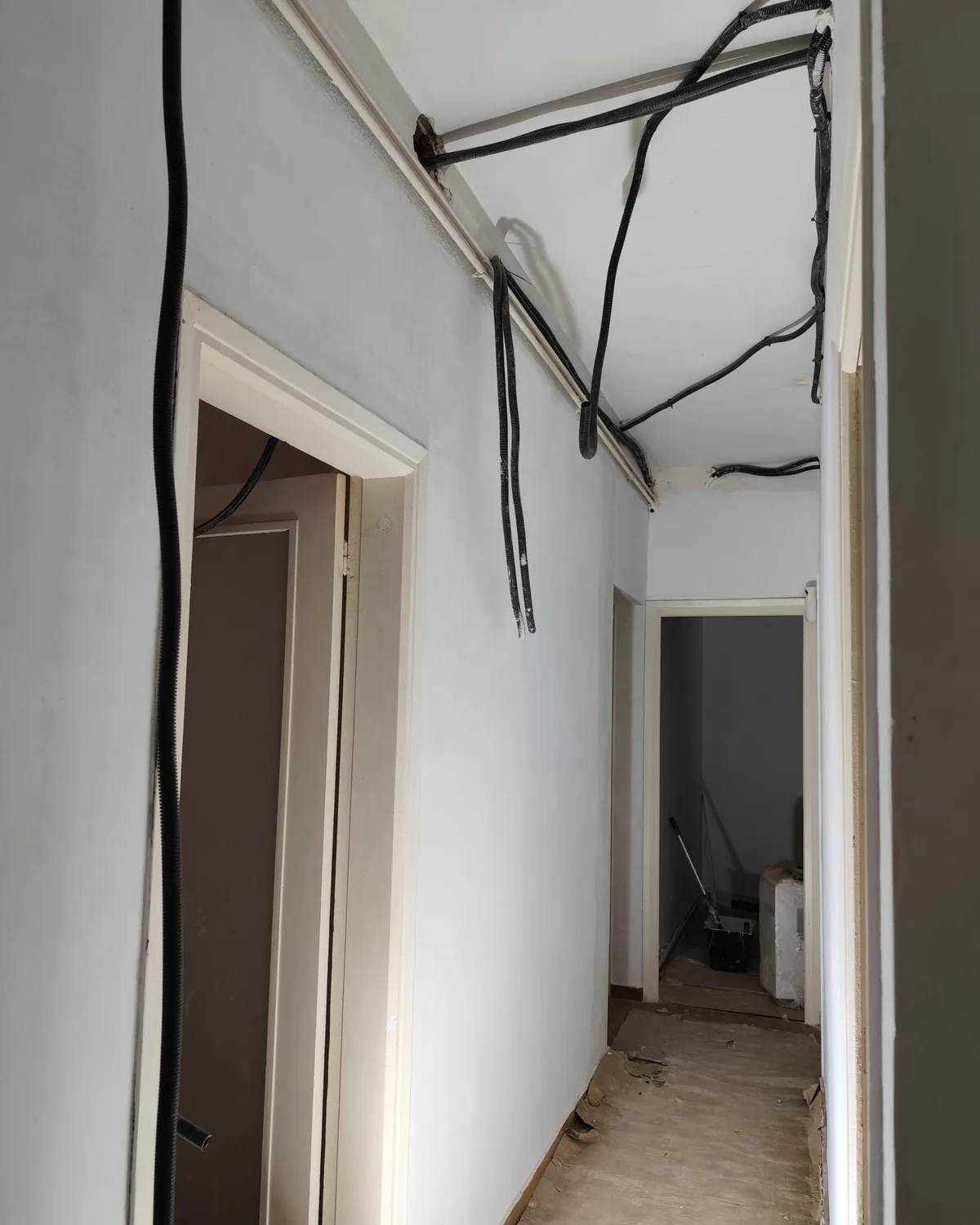Pasillo de una vivienda en obra con el cableado eléctrico nuevo bajando del techo antes de cerrar