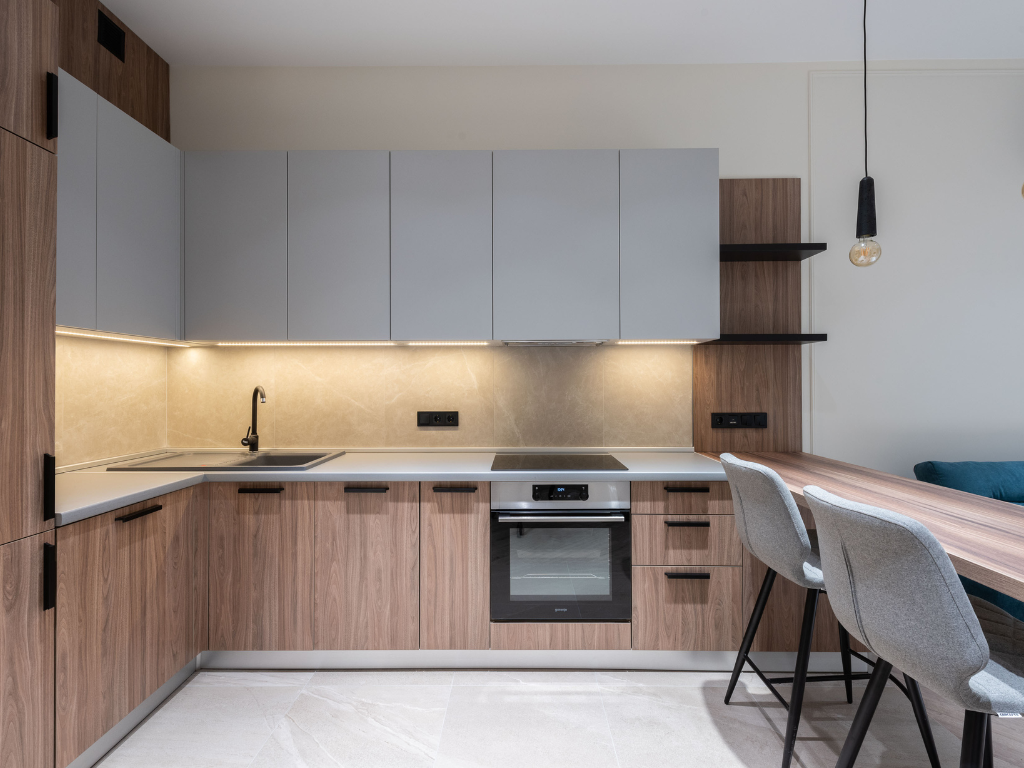 Cocina moderna con mobiliario en madera y muebles superiores grises en un piso reformado en el Eixample.