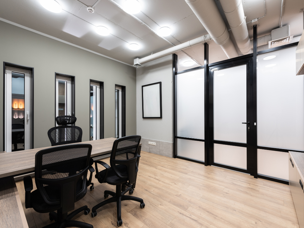 Oficina moderna con pavimento continuo y salas acristaladas en estilo industrial elegante.