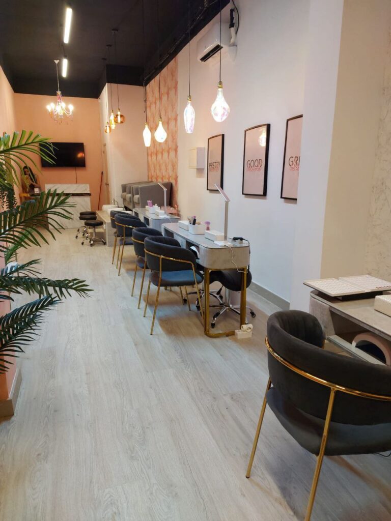 Interior de un centro de estética con puestos de manicura, sillas de terciopelo y decoración cálida.