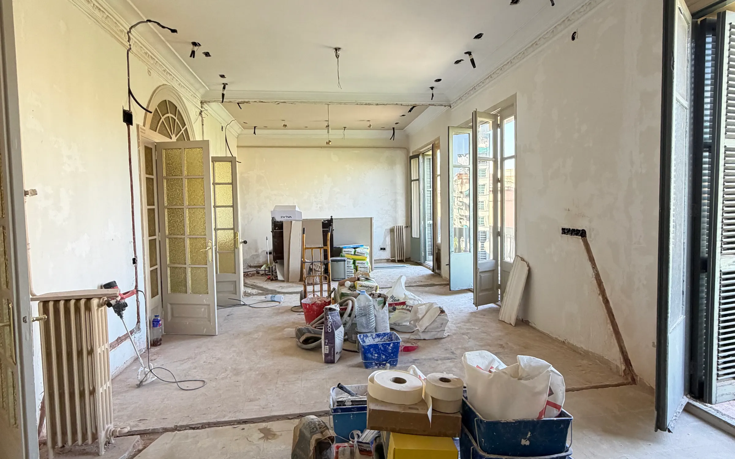 Saló d’un habitatge de l’Eixample en obra, amb les motllures del sostre, la porta envidrada d’arc i les balconeres al carrer
