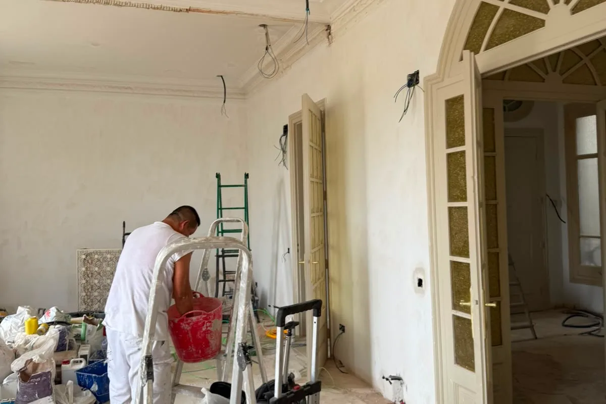 Pintor treballant al saló de Gran Via al costat de la porta d’arc envidrada i les motllures conservades