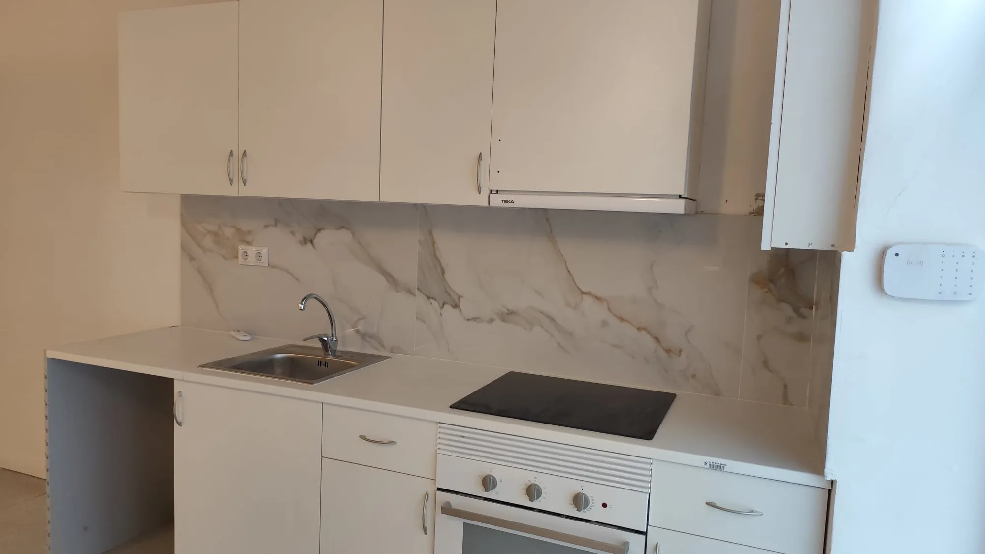 Cuina lineal blanca acabada amb taulell i placa nous en una reforma d’Obrescat a l’Eixample, Barcelona