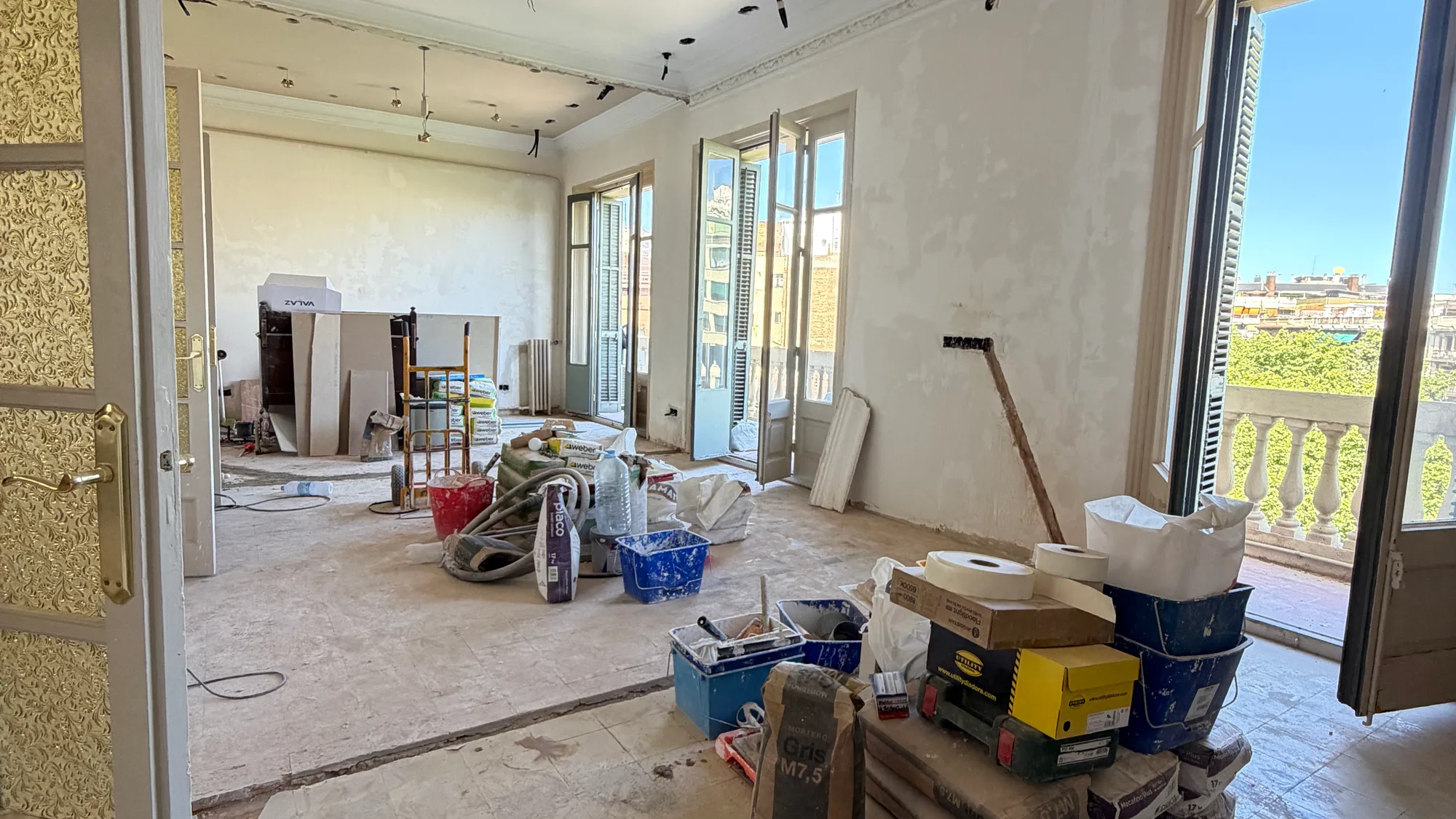 Saló d’un habitatge en obra amb les balconeres obertes sobre les teulades de Barcelona