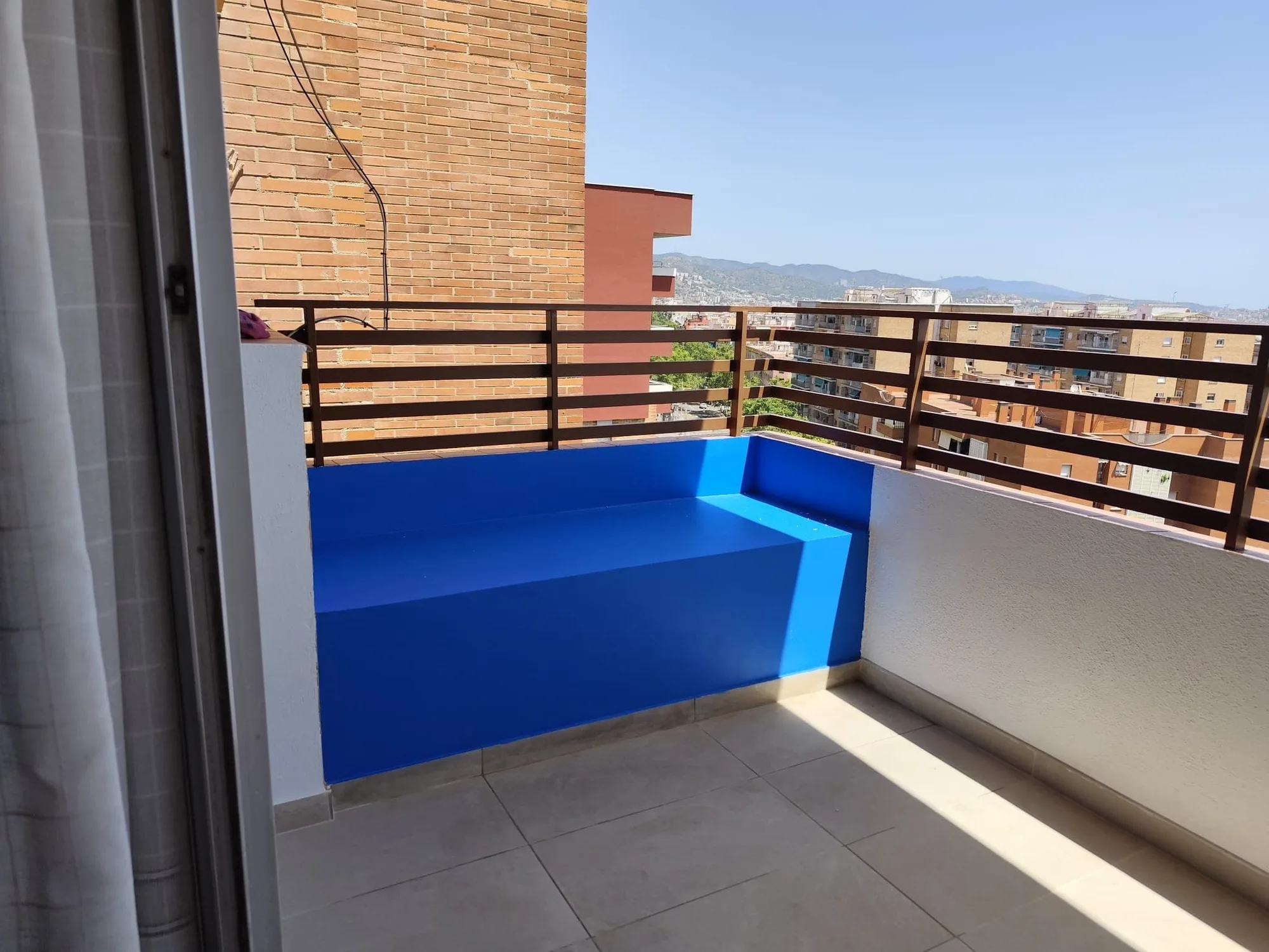 Terraza con un banco de obra pintado de azul, suelo de baldosa y barandilla de listones de madera