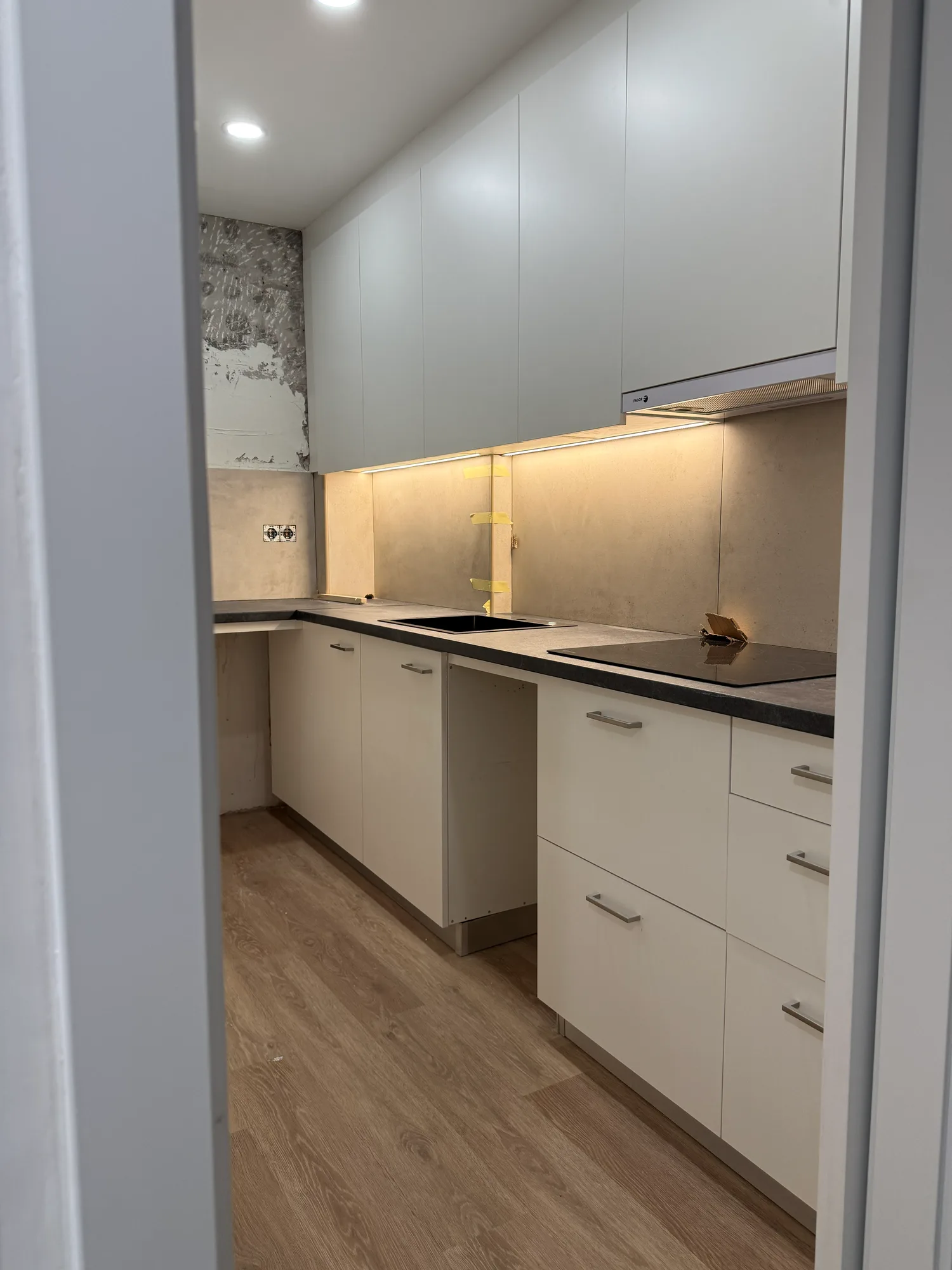 Cocina en montaje, con muebles claros, encimera oscura, placa de inducción y tira de luz bajo los muebles altos
