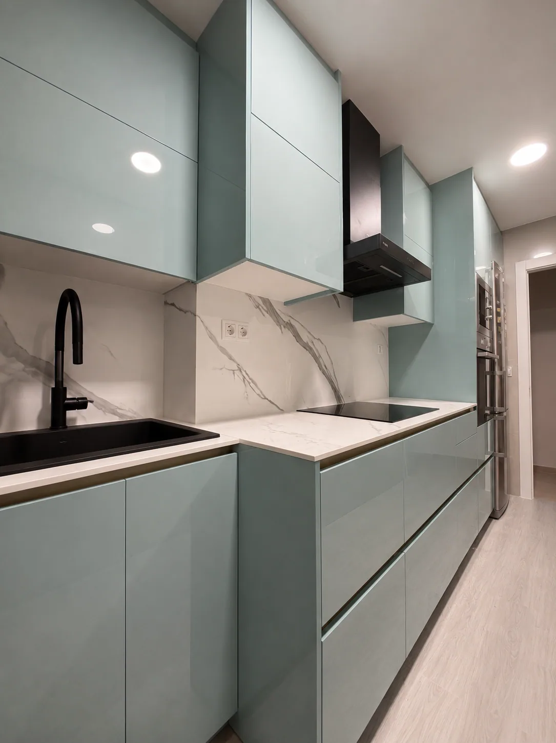 Cocina en línea terminada, con frentes verde agua, encimera clara y campana negra