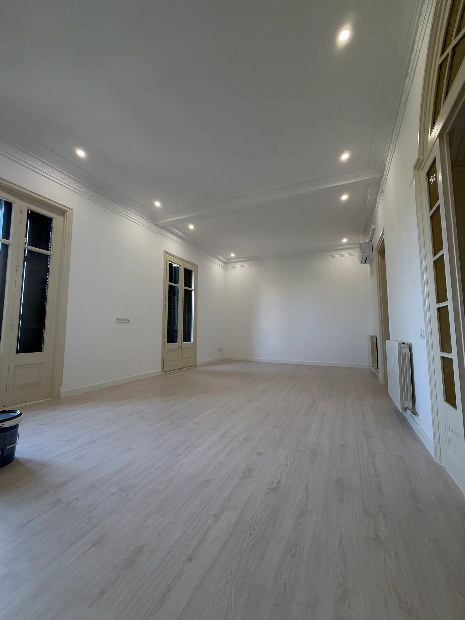 Salón diáfano de una vivienda terminada, con suelo laminado claro y focos empotrados