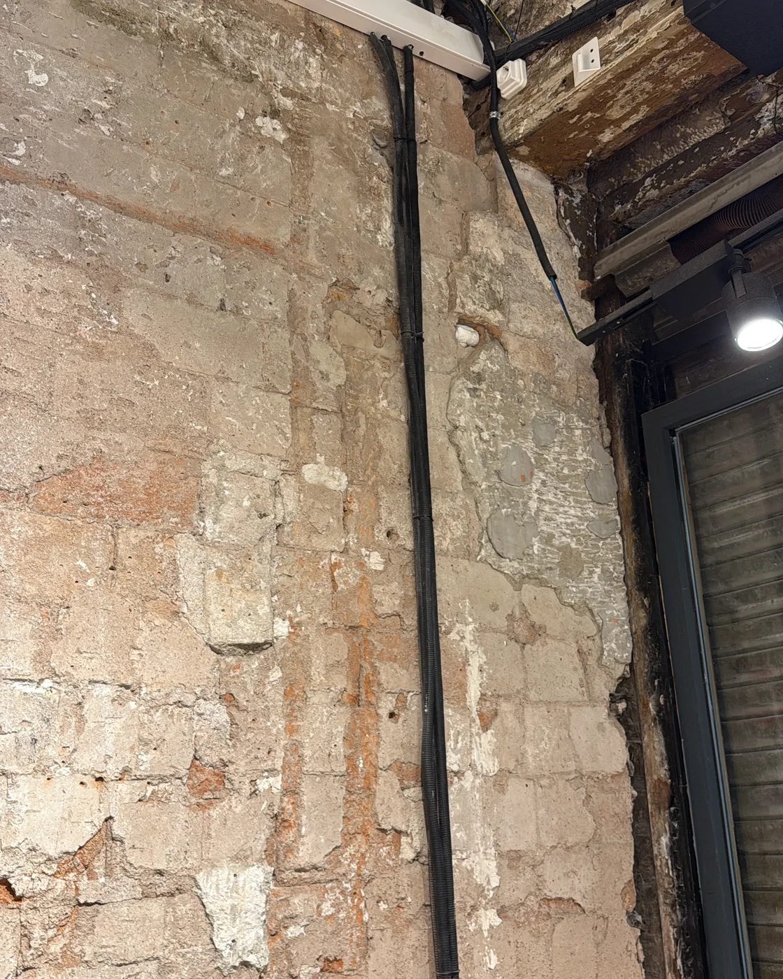 Pared de piedra antigua recuperada junto a la viga de madera y la nueva canalización eléctrica, rehabilitación en Barcelona